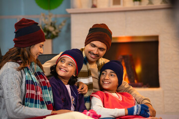 Happy family in winter wear spending time together at weekend holidays near fireplace at home - concept of relationship bonding, parenthood and togetherness
