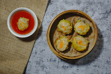Steamed Dumpling Siew Mai served in a bamboo basket steamer with dipping sauce isolated on grey background. Flat lay.