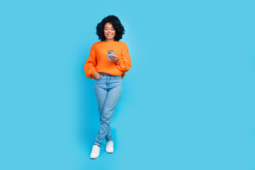 Fototapeta na wymiar Full body photo of pretty young girl hold gadget eshopping order wear trendy knitwear orange outfit isolated on blue color background