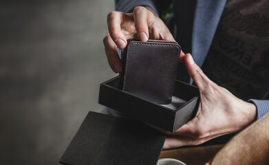 The man's hands take out a dark brown leather wallet from a black gift box. An elegant accessory...