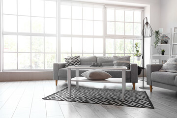 Interior of light living room with grey sofas and coffee table near big window