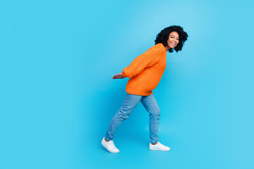Fototapeta na wymiar Full body photo of pretty young girl carry big empty space walking dressed stylish knitted orange outfit isolated on blue color background