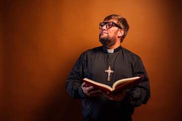 Portrait of a priest with crucifix and black shirt holding a bible.