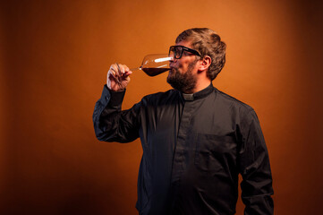 Portrait of a priest with crucifix and sunglasses drinking wine.