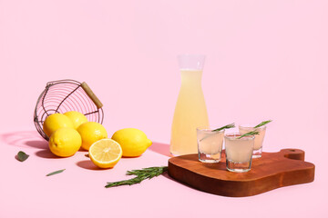 Jug and shots of tasty Limoncello with rosemary on pink background