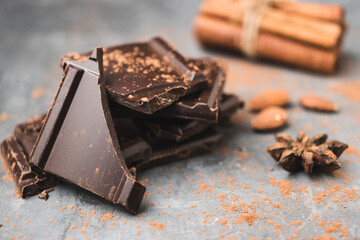 Heap of delicious dark chocolate pieces or cubes, chopped, broken chocolate bar, almond nut, cinnamon sticks and star anise on a dark background