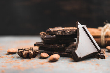 Heap of delicious dark chocolate pieces or cubes, chopped, broken chocolate bar, almond nut, cinnamon sticks and star anise on a dark background