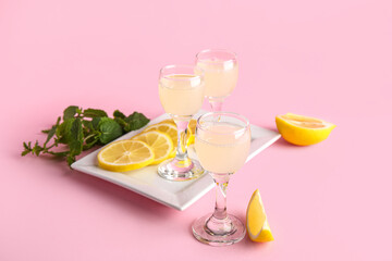 Glasses of tasty Limoncello and plate with sliced lemon on pink background