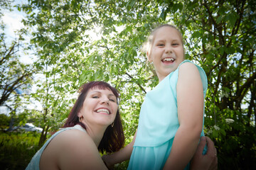 Fototapeta premium Happy mother and daughter enjoying rest, playing and fun on nature on a green lawn and with a blooming apple tree in the background. Woman and girl resting outdoors in summer and spring day