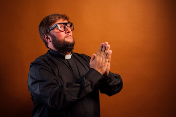 Portrait of a priest with crucifix and black shirt praying.