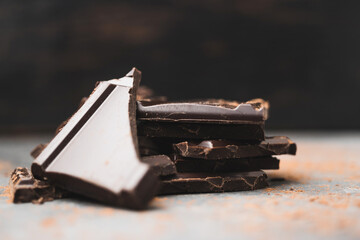 Heap of delicious dark chocolate pieces or cubes, chopped, broken chocolate bar on a dark background
