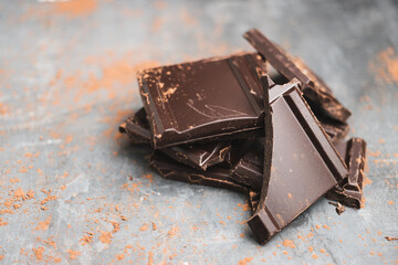 Heap of delicious dark chocolate pieces or cubes, chopped, broken chocolate bar on a dark background