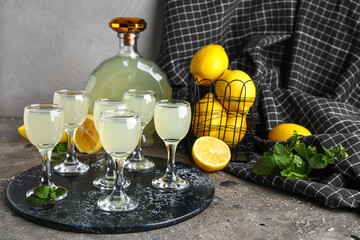 Board with glasses and bottle of tasty Limoncello on grey table