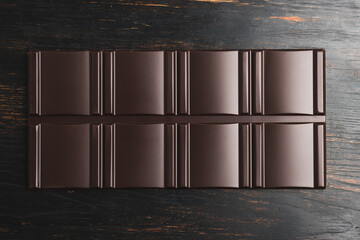 Delicious dark chocolate bar on a dark wooden background, top view