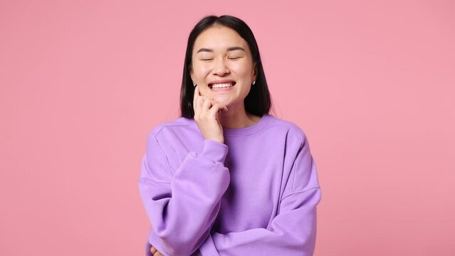 Young woman of Asian ethnicity wear purple sweatshirt look around think dream put hand prop up on chin lost in thought and conjectures isolated on plain pastel light pink background. Lifestyle concept