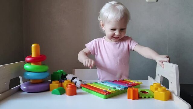 Funny cute child girl plays on a colored xylophone and makes a funny face. Educational toys for small children. A little girl under two years old explores toys.