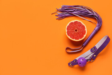 Whip and mouth gag from sex shop with half of tasty grapefruit on orange background
