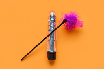 Vibrator and feather stick from sex shop on orange background