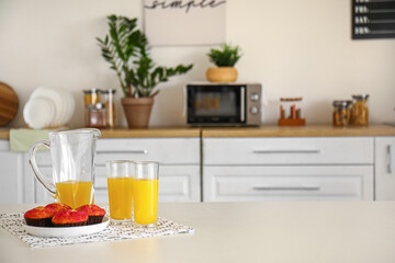 Fototapeta na wymiar Jug and glass of fresh orange juice with muffins on table in kitchen