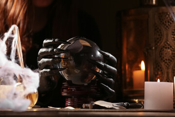 Witch with crystal ball at dark wooden table, closeup