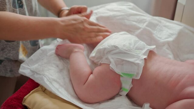 The hands of a masseur rub the babys feet on the changing table. the baby is wearing a diaper. no faces are visible. massage for the first year of life.