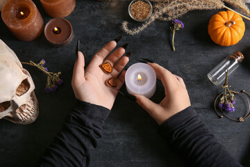 Witch with burning candle on dark table