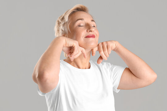 Beautiful mature woman doing face building exercise on light background, closeup