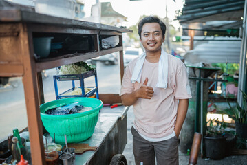 asian seller standing behind traditional food cart with thumb up gesture