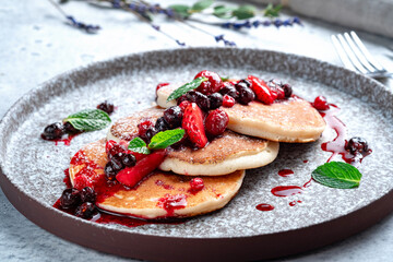 Sweet pancakes with jam and wild berries in a gray plate decorated with powdered sugar and mint, close up