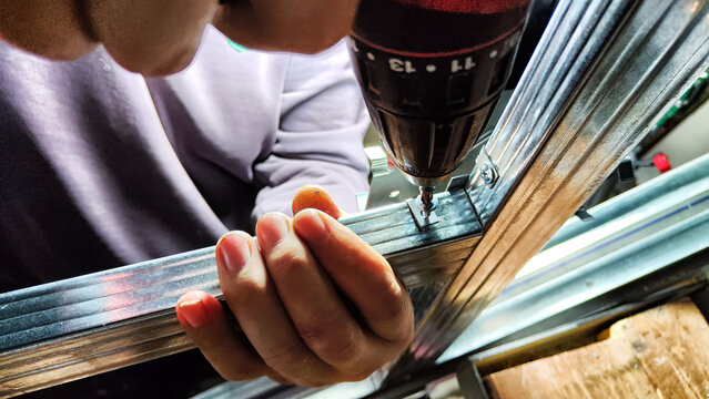 Man hands drilling metal planc in construction. Building iron fence with a drill and screw. Close up of his hand and the tool drill