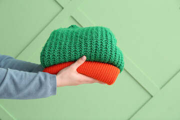 Female hands with stack of different stylish sweaters on green background
