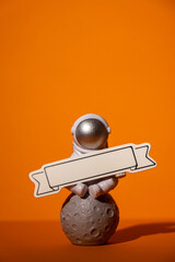Plastic toy astronaut with paper note template mock up for your text on colorful orange background...