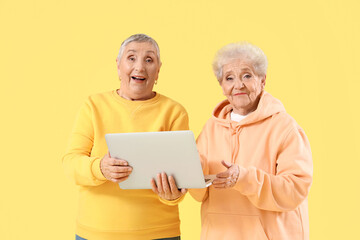 Senior female friends with laptop on yellow background