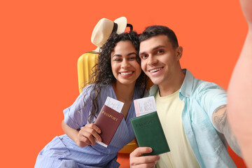 Couple of tourists with passports taking selfie on orange background