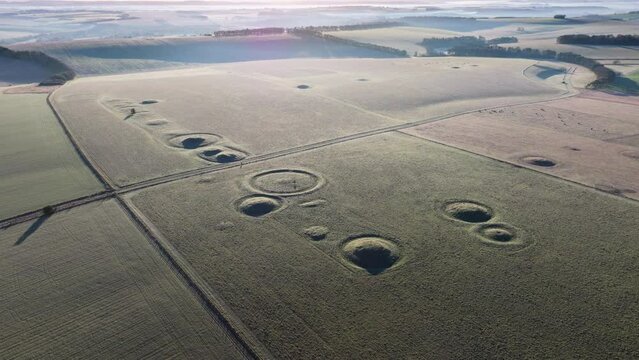 Wide high establishing aerial shot of burial mounds and barrows in low sun, Salisbury, UK