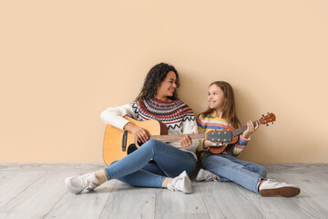 Obraz na płótnie Canvas Young woman and girl playing acoustic guitars together on beige background