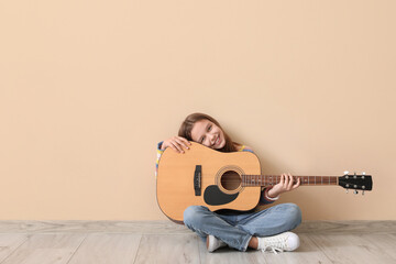 Teenage girl with acoustic guitar on beige background