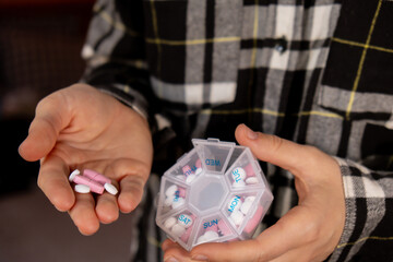 Female hands sorting pills Organizer weekly shots Closeup of medical pill box with doses of tablets for daily take medicine with white pink drugs and capsules. Young woman getting her daily vitamins