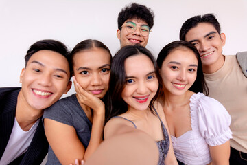 A diverse group of six happy young friends taking a group selfie with a smartphone, smiling and enjoying togetherness.