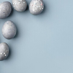Festive Easter background. Gray-blue Easter eggs with stars on a blue table. Card with a place for text. Top view.