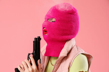 Beautiful young stylish woman in balaclava with gun on pink background - obrazy, fototapety, plakaty