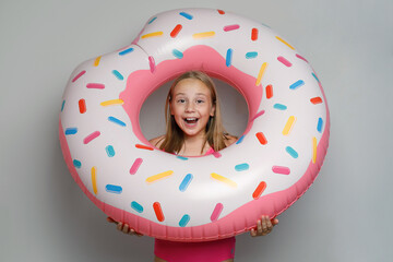 Excited child girl with pink rubber inflatable ring swimming pool float standing on white studio wall background