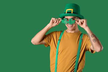 Happy young man in leprechaun's hat wearing party glasses on green background. St. Patrick's Day