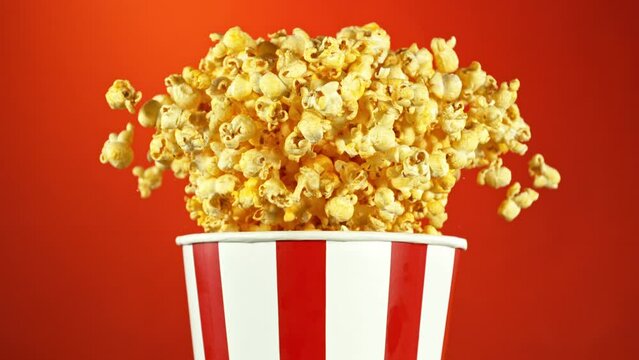 Super Slow Motion of Exploding popcorn from Bucket. Isolated on Red Background. Studio Shot of Flying Food. Filmed on High Speed Cinema Camera, 1000fps.