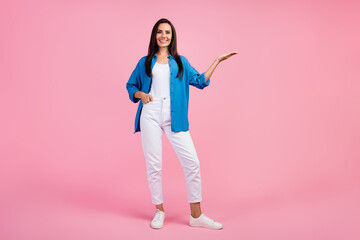 Full size photo of adorable lovely girl dressed blue shirt white trousers arm show object empty space isolated on pink color background