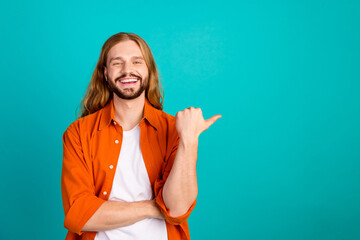 Portrait of optimistic man with long hair dressed orange shirt indicating at proposition empty...