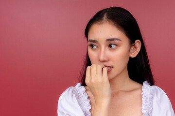 An anxious and jittery young Asian woman biting her nail with a look of concern against a vibrant...