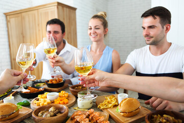 Friends with white wine toasting over served table with food