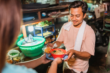 asian male seller giving customer a bowl of indonesian fried noodle