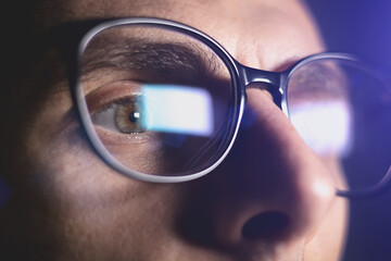 Man works on internet. Reflection at the glasses from laptop..Close up of man's eyes with black female glasses for working at a computer. Eye protection from blue light and rays.
